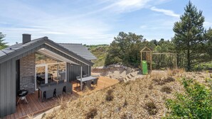 Ein modernes Haus mit Terrasse, Grill und einer Holz-Spielanlage.