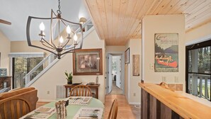 Un espace repas comprenant une table en bois, des chaises, un lustre et un escalier menant à un autre niveau.