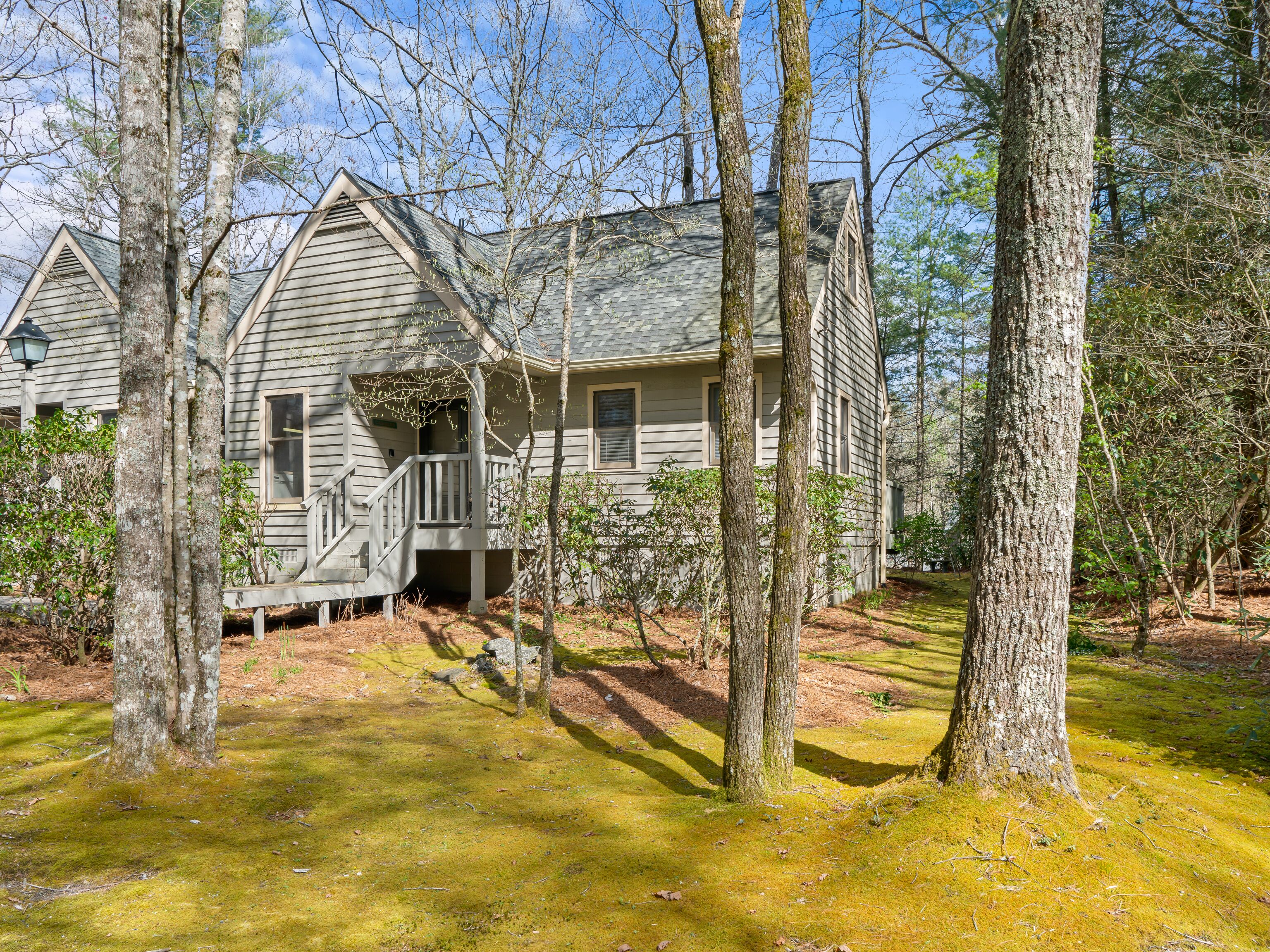A two-story cabin with a porch, surrounded by trees and a grassy yard.