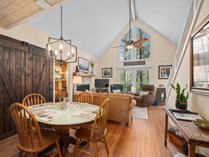 A spacious loft-style living area with a high ceiling, wooden flooring, a dining table with chairs, a sofa, and a ceiling fan. - Peaceful Retreat w/ Loft in Nantahala National Forest. ⛷ 🛶 (Sapphire)
