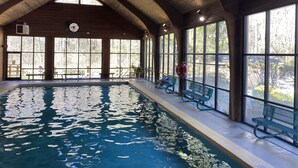 Une piscine intérieure à l’eau claire, entourée de grandes fenêtres et de bancs.