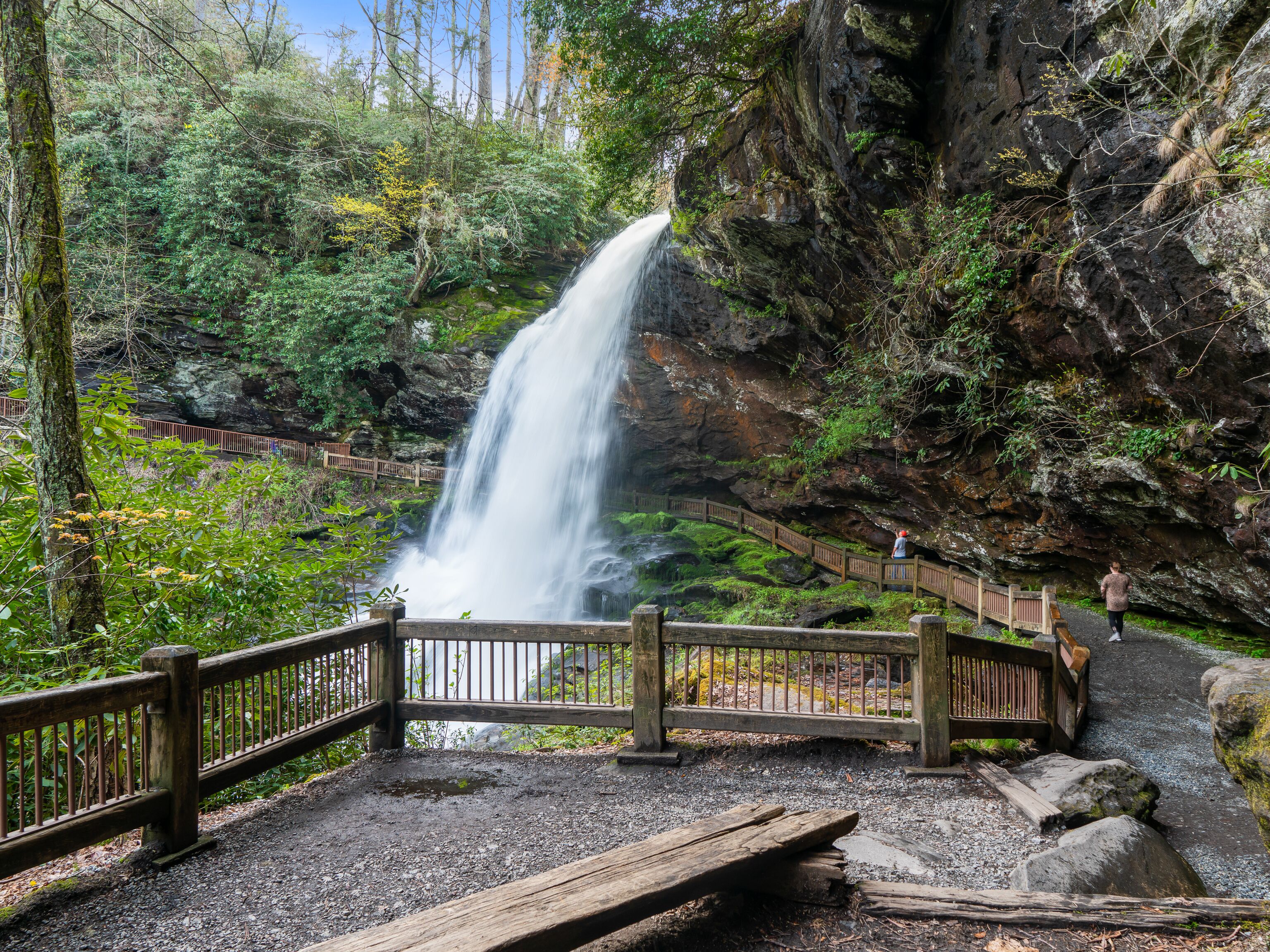 A waterfall in a forested area with a wooden walkway and railing.