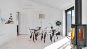 Un espace repas moderne avec une table et des chaises en verre transparent, une suspension et un poêle à bois.