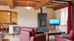 A living room with a fireplace, leather sofas, a television, and a dining area with a table and chairs. - 4 bedroom pet friendly home in Portbail (Portbail)