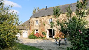 A stone house with a gravel driveway, a front door, and a table with chairs outside. - 4 bedroom pet friendly home in Portbail (Portbail)