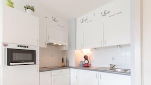 Een moderne keuken met witte kastjes, een ingebouwde oven, een magnetron, een spoelbak en een koffieapparaat.