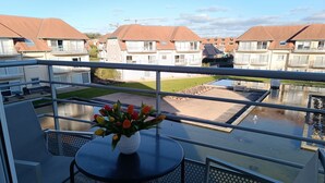 Een balkon met een tafel en stoelen, een bloevas en uitzicht op een woonwijk met huizen en een zwembad.