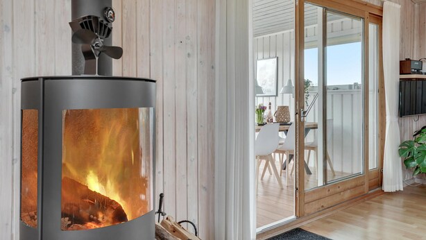 Et moderne interiør med en brændeovn, trævægge, en skydedør til et udendørs område samt et spisebord med stole.