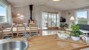 Et moderne køkken med en central ø, et spiseområde med træstole, en sofa og et fjernsyn.