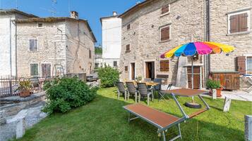 Un cortile con edifici in pietra, posti a sedere all'aperto e un ombrello colorato.