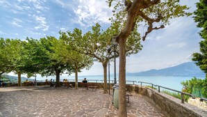 A stone-paved terrace with benches and trees overlooking a body of water and distant mountains.
