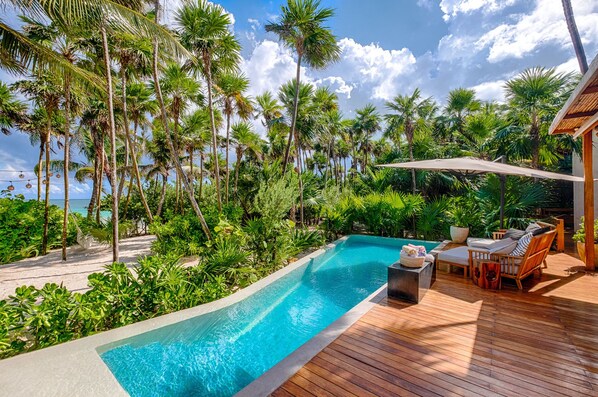 A poolside area with a wooden deck, lounge chairs, and an umbrella. - Fully serviced luxury beachfront villa in Tulum
(Sian Ka'an)