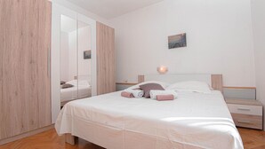 Ein Schlafzimmer mit einem Bett, einem Nachttisch, einer Wandleuchte, einem Spiegel und einem Holzschrank.