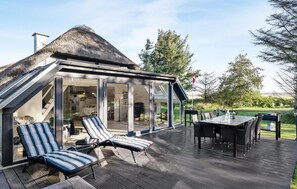 A modern house with a glass-enclosed patio, outdoor seating, and a thatched roof. - 3 bedroom gorgeous home in Ringkøbing (Ringkøbing)