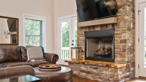 A living room with a stone fireplace, leather sofa, and a television mounted above it.