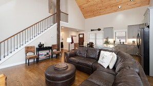 A spacious living area with a brown leather sectional sofa, a round ottoman, and a staircase with a wooden railing.