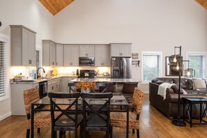 A modern kitchen with grey cabinets, a central island, and a dining area with wicker chairs and a glass table.