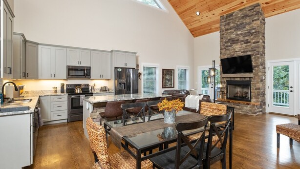 A spacious kitchen with modern appliances, a dining area with wicker chairs, and a stone fireplace.