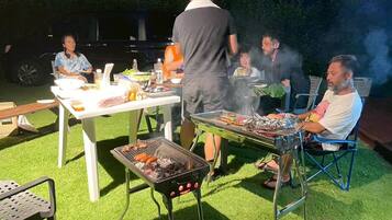 An outdoor barbecue with people grilling and sitting around a table with food and drinks.