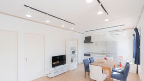 Una sala de estar moderna y bien iluminada con un televisor de pantalla plana, una mesa de comedor con sillas y una cocina con armarios y electrodomésticos.
