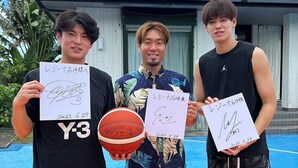 Tre persone che tengono palloni da basket firmati e documenti su un campo da basket.
