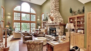 Un salón espacioso con chimenea de piedra, ventanas amplias y una estantería de madera.