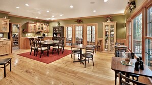 Una cocina amplia con armarios de madera, un comedor con alfombra roja y ventanas grandes que dejan entrar luz natural.