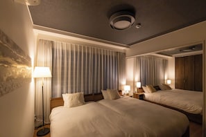 Two spacious beds with bedside tables and lamps, set against a textured backdrop with a large window offering a view.