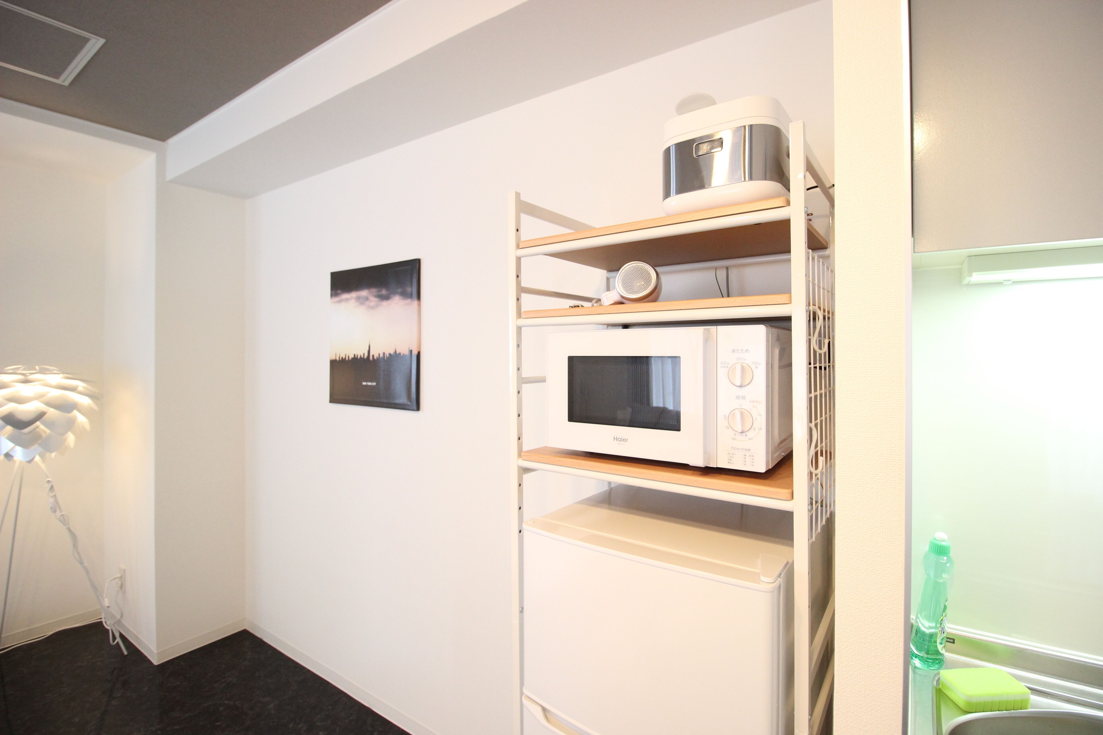 A compact kitchenette with a microwave, a kettle, and a shelf unit.
