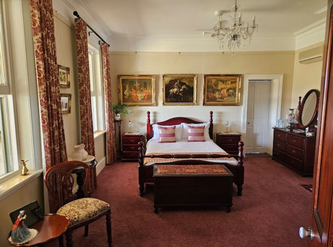 A bedroom with a large bed, a wooden chair, a dresser, and a chandelier.