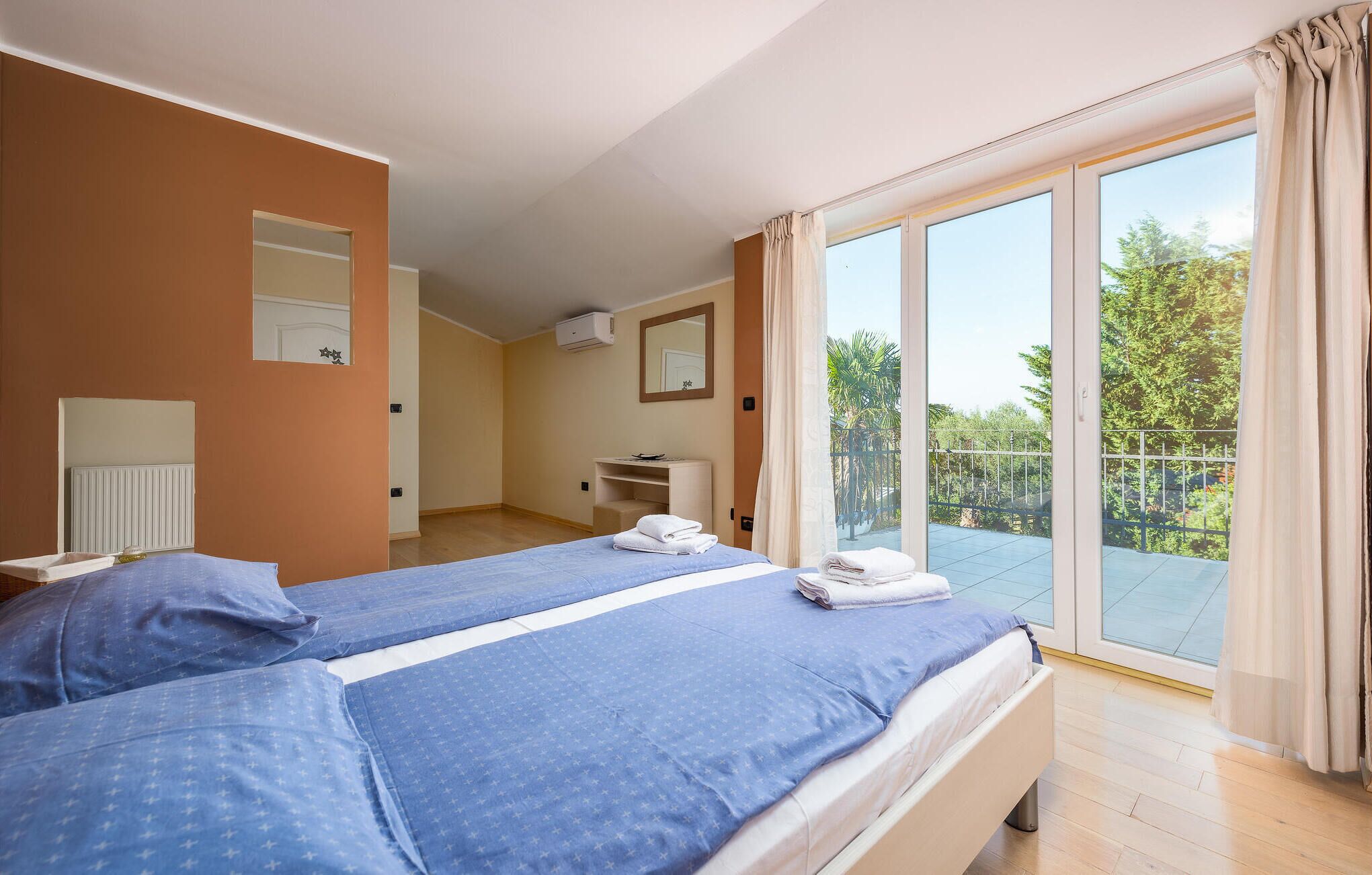 A hotel room with a large bed, a bathroom, and a balcony with a view of trees.