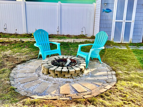 A circular fire pit with two blue Adirondack chairs facing each other, surrounded by a stone border.
