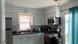 Une cuisine avec des meubles blancs, un réfrigérateur en acier inoxydable, un four à micro-ondes, une cuisinière et un évier.