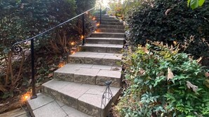 Eine steinerne Treppe mit Metallgeländern, umgeben von üppigem Grün und einem Gebäude im Hintergrund.