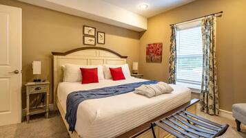 A hotel room with a large bed, a bench, a nightstand, a window with curtains, and artwork on the wall.