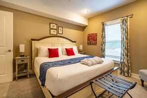 A hotel room with a large bed, a bench, a nightstand, a window with curtains, and artwork on the wall. - 2 King Beds, Outdoor Fireplace and Air Hockey (Canton)