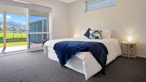 Une chambre à coucher avec un lit, une table de chevet, une fenêtre avec des stores et une vue sur un paysage verdoyant.