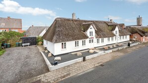 A traditional white building with thatched roofs, a paved driveway, and a small garden area with rocks and plants. - Gorgeous home in Højer with WiFi (Højer)