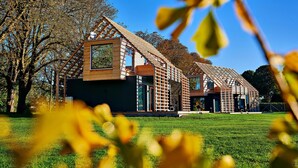 Une maison moderne en bois, dotée d’un toit en pente, de grandes fenêtres et d’un balcon apparent.
