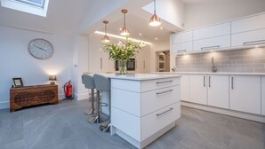 Una cocina moderna con armarios blancos, iluminación colgante, una isla central y un extintor.