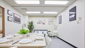A dining area with a long table set for a meal, framed pictures on the walls, and a potted plant.