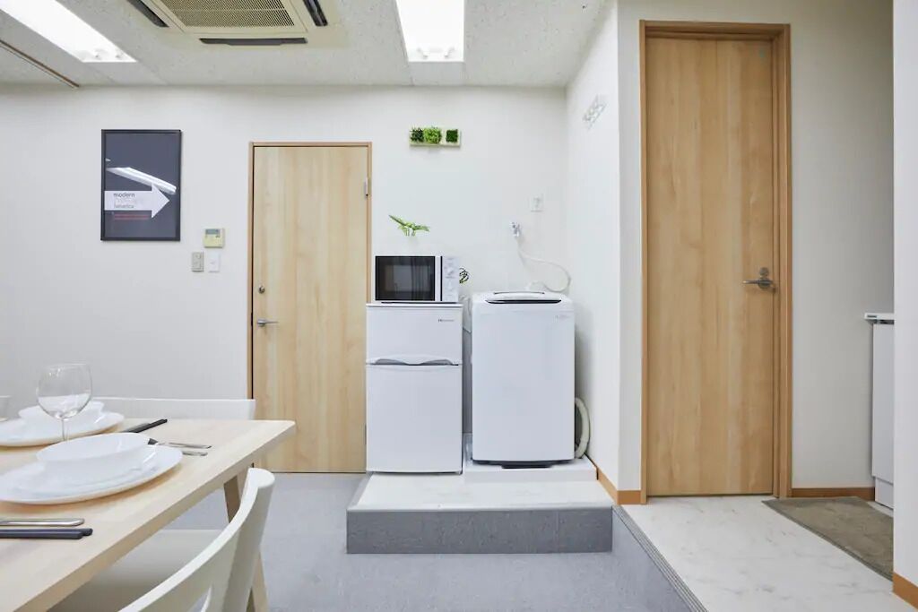 Cozinha moderna com eletrodomésticos brancos, porta de madeira e uma pequena planta na parede.
