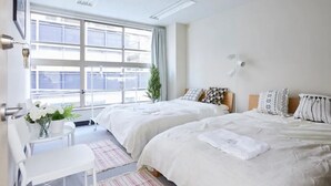 Quarto de hotel com duas camas, uma escrivaninha e janela com vista.