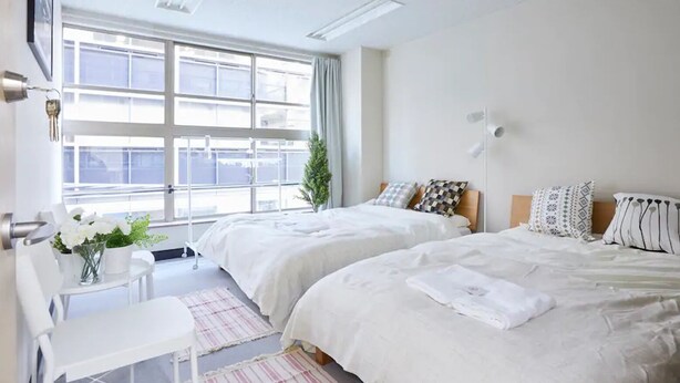 A hotel room with two beds, a desk, and a window with a view.
