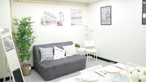 A modern room with a grey sofa, a dining table set with plates and cutlery, a potted plant, and framed artwork on the walls.