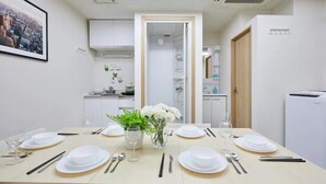A dining room with a table set for six, white plates, cutlery, and a vase with flowers. - TORA HOTEL Taito B (Tokyo)