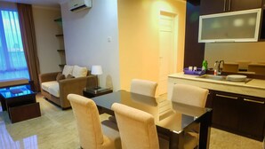 A modern living room with a sofa, a dining table with chairs, a TV mounted above the kitchen counter, and a small kitchen area with a sink and dish rack. - Fantastic View 2BR Apartment at FX Residence Sudirman (Jakarta)