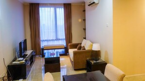 A hotel room with a sofa, a TV, a small table, and a window with curtains. - Fantastic View 2BR Apartment at FX Residence Sudirman (Jakarta)
