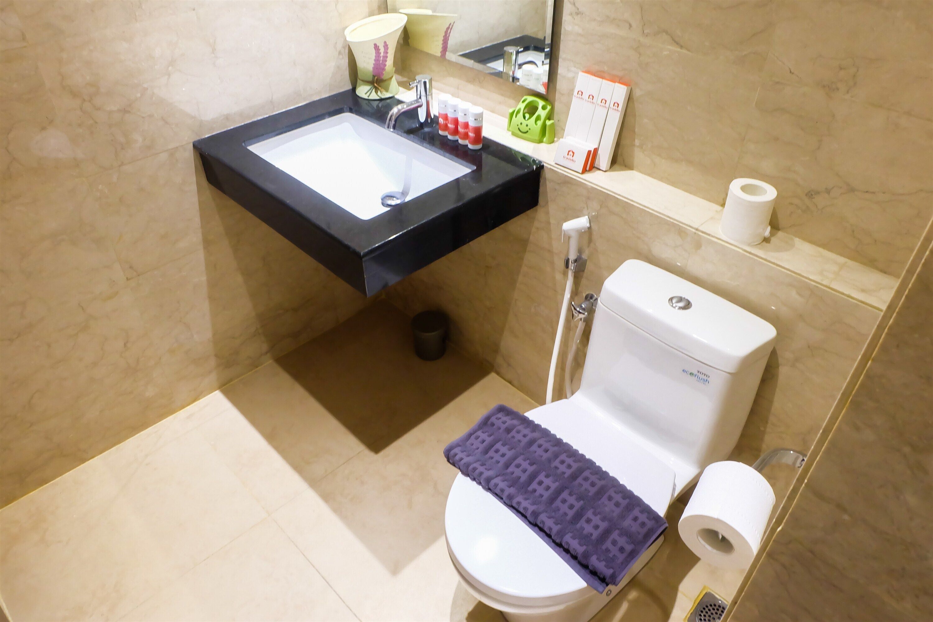 Un baño con un lavabo negro, un inodoro blanco y una alfombrilla morada.