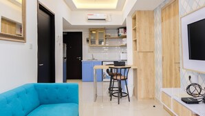 A modern living room with a blue sofa, a dining area with a table and chairs, a kitchen with blue cabinets, and a TV mounted on the wall. - Nice and Prime Location 1BR Casa De Parco Apartment (Pagedangan)